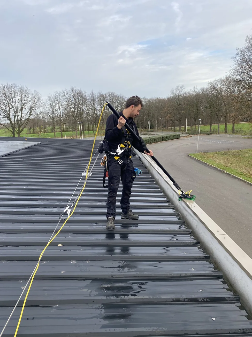 Medewerker met veiligheidsharnas reinigt zonnepanelen en dakrand op hoogte